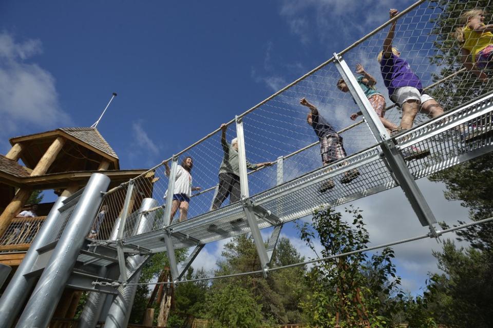 People crossing a suspended metal walkway between large wooden structures at The Wild Center in Tupper Lake NY