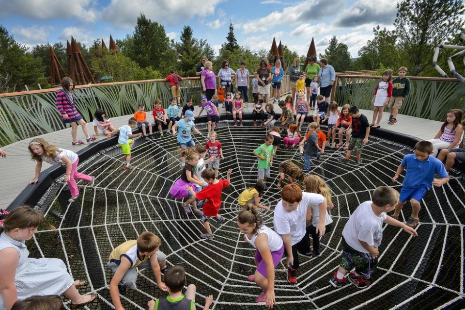 Dozens of children playing on the outdoor spiderweb exhibit