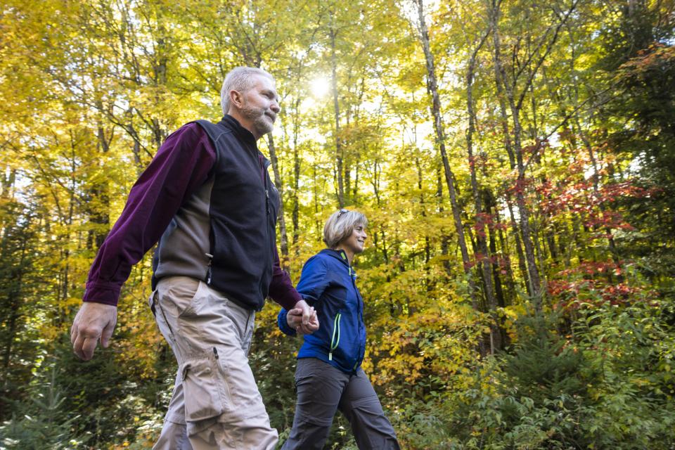 A gray-haired couple strides through bright, fall foliage-covered forest.