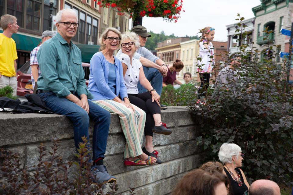 People sit on a brick wall at Berkeley Green in downtown Saranac Lake on a warm day