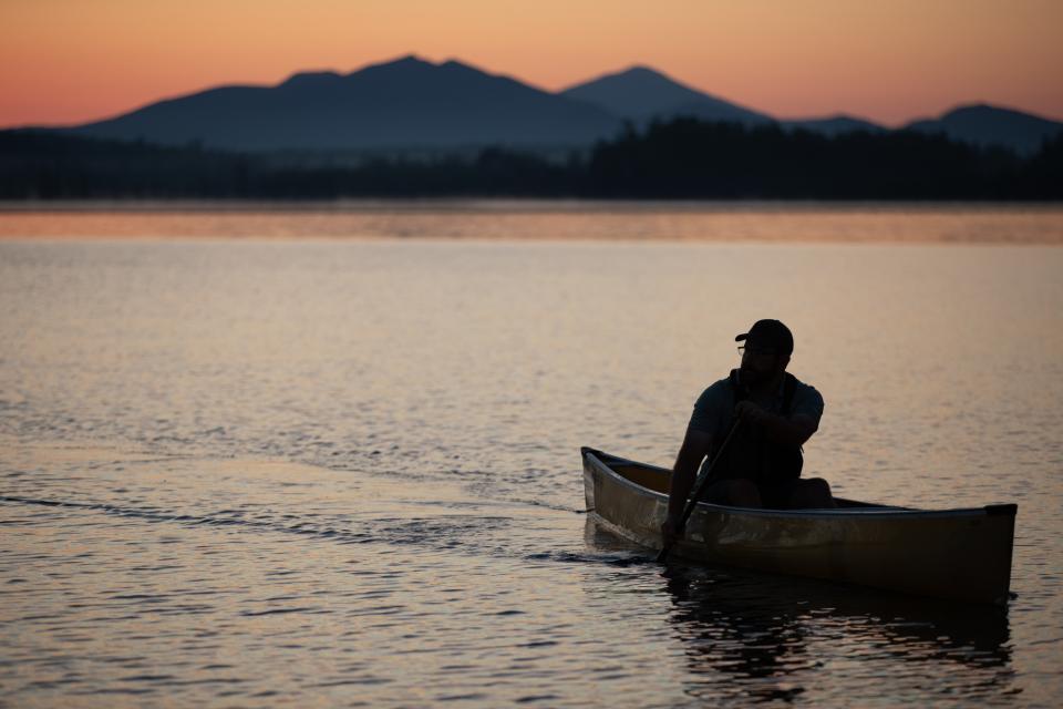 A single-person canoe paddling in the sunset