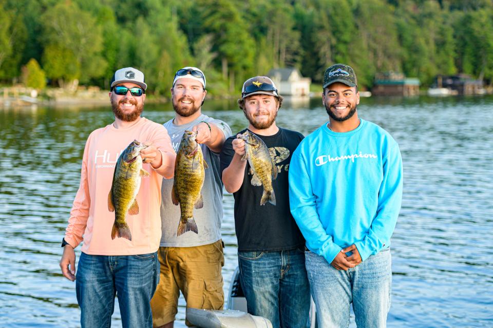 A group of friends in fishing hats and shirts hold up fish four a photo.