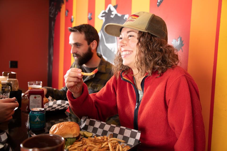A woman in a trucker hat smiles while eating a french fry.