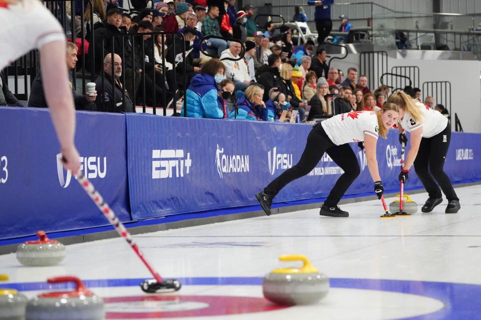 Female curling athletes compete on an icy curling rink.