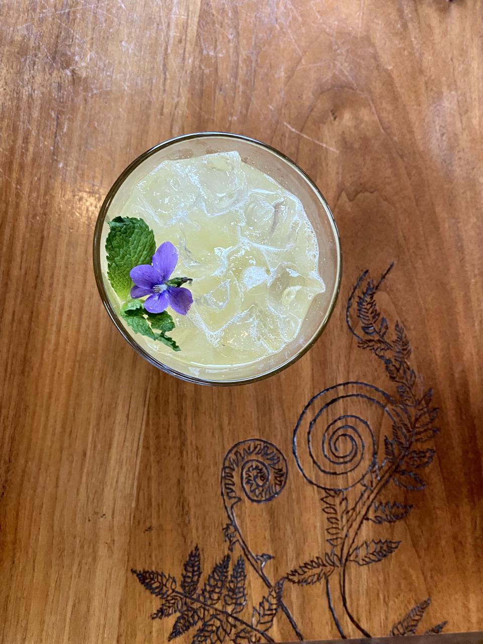 lemonade with flower garnish on table with wood carving of a fiddlehead fern