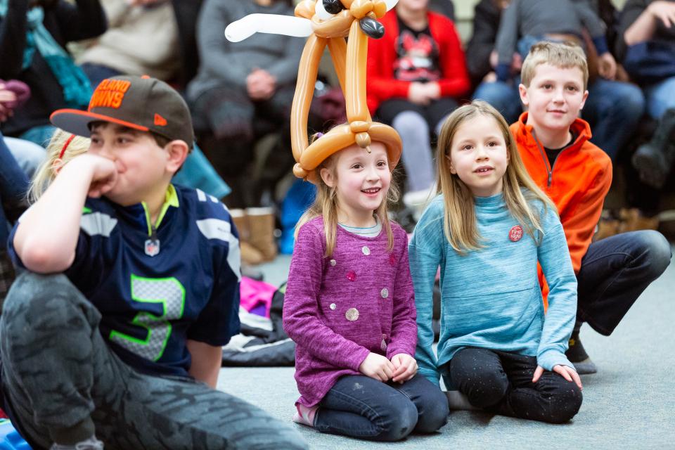 Children wearing balloon hats laugh at an outdoor event.