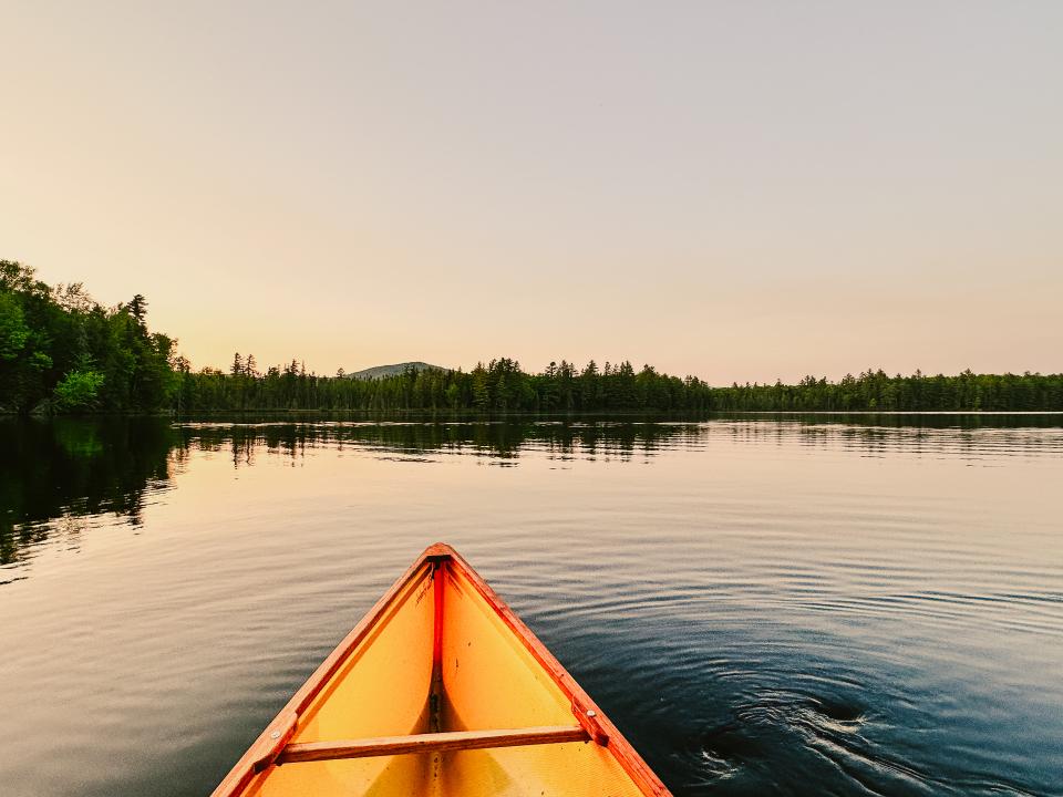 The bow of a canoe on a placid pond with the shore and a mountain in the distance