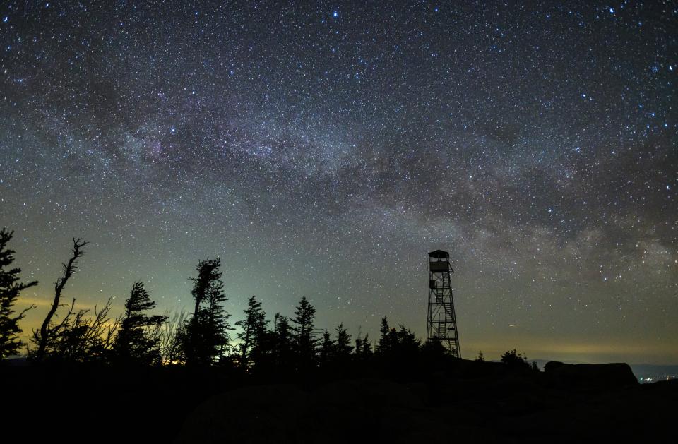 A nighttime image of the fire tower on Hurricane Mountain, with the Milky Way glowing bright against the dark sky