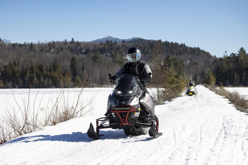 A snowmobiler rides on a straight-away in between ponds in winter.