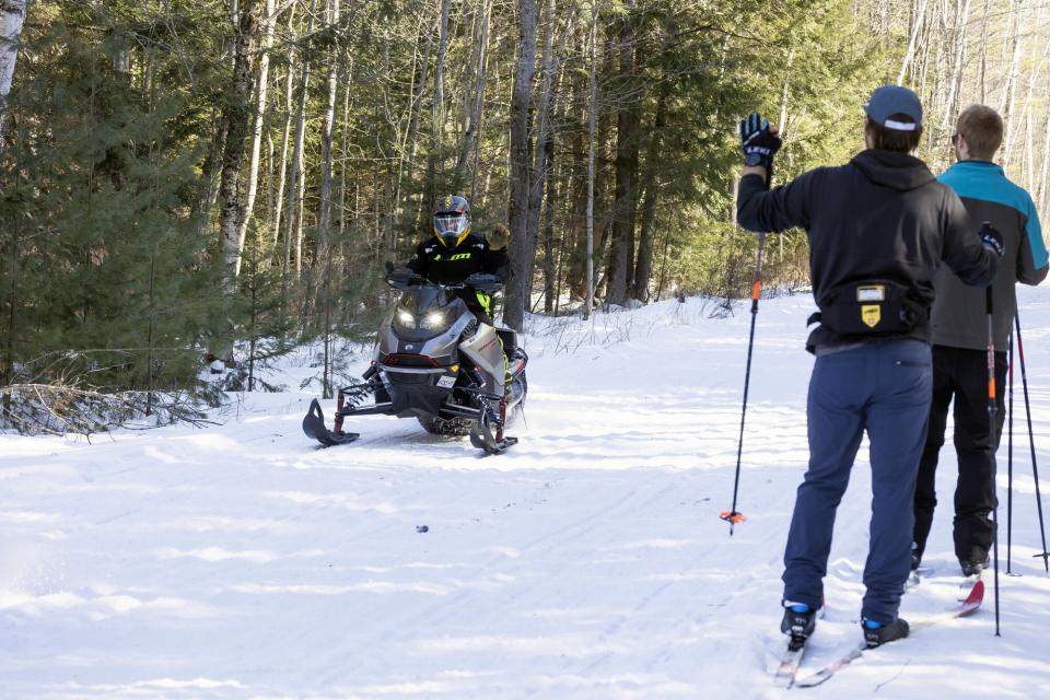 a snowmobiler passes two cross-country skiers on a snow-covered trail.