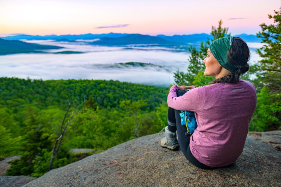 A woman sits on top of Baker Mountain and watches the sun rise