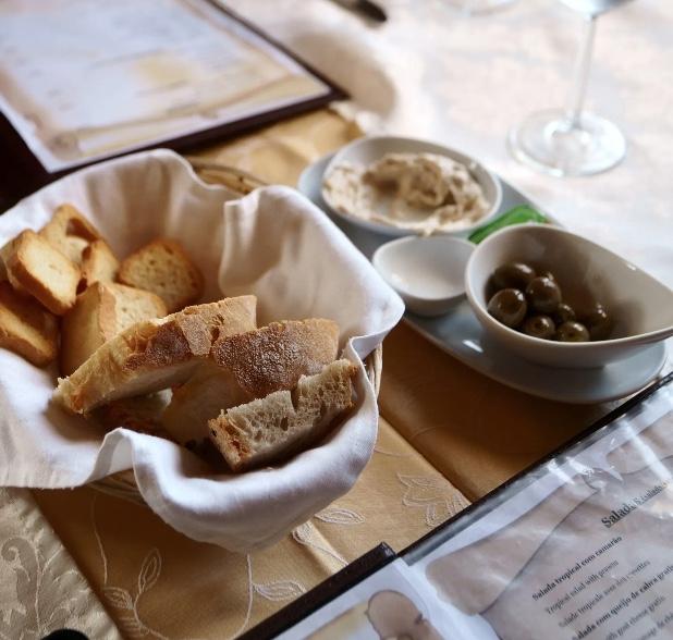 A basket of bread with a butter dish and olives on the side.