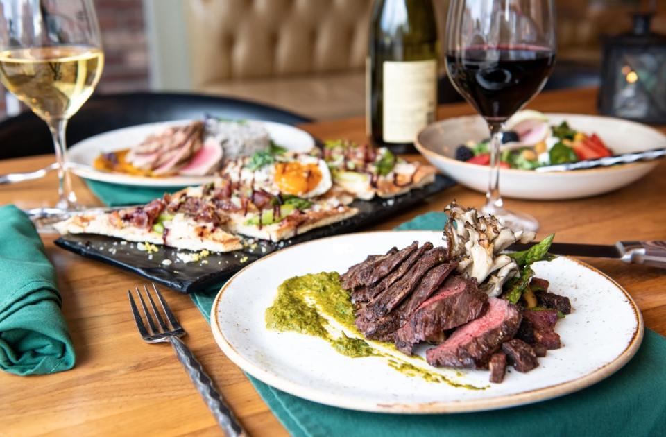 a spread of steak and mushrooms, with a flatbread appetizer and wine glasses on the table.
