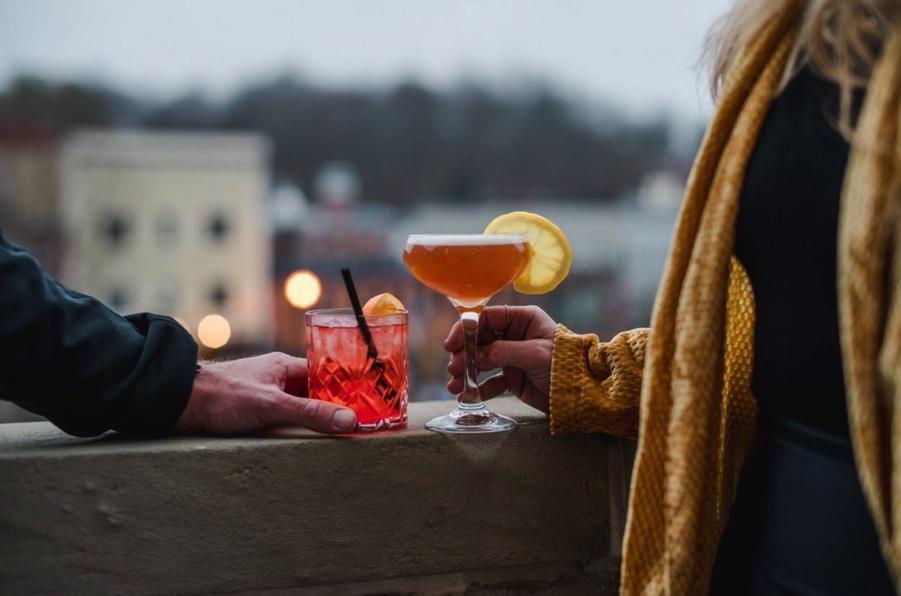 A man and woman hold cocktails on the balcony of a hotel.