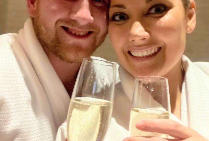 Two people in spa bath robes drink champagne while waiting to get a massage