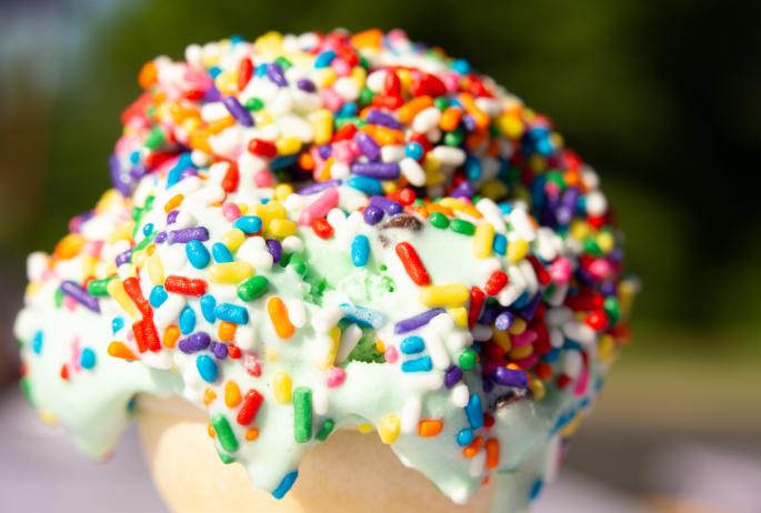 Extreme close-up of a melting ice cream cone covered in rainbow sprinkles.