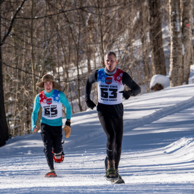 Two participants in winter sports race over snow in the Empire State Winter Games. One athlete is in a blue shirt and snowshoes
