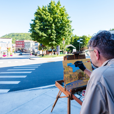 An artist stands at an easel on a sunny sidewalk