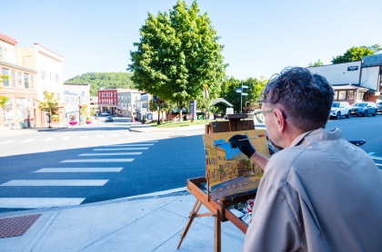 An artist stands at an easel on a sunny sidewalk