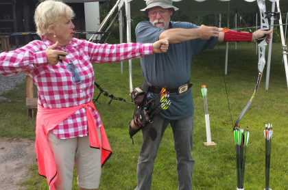 A man demonstrates how to draw a bow properly while a woman mimics without a bow