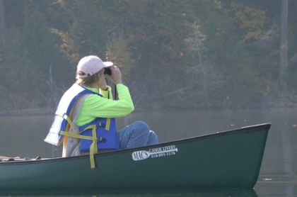 Person in a canoe on the water observing the distance through binoculars