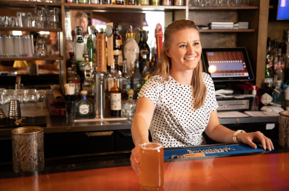 A woman behind the bar serves a beverage and smiles