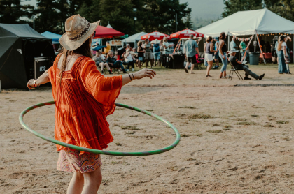 Woman in red dress and straw hat hula hoops in front of smallfestival crowd