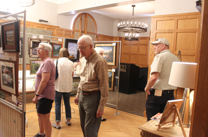 People observe the art inside a large room with wood paneled walls at the guide boat art show