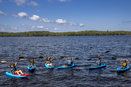 A group of kayakers hold their paddles above their heads in triumph.