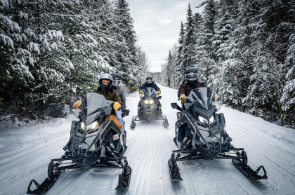 the fleet of Polaris machines riding down a freshly groomed trail lined with snow-covered pines