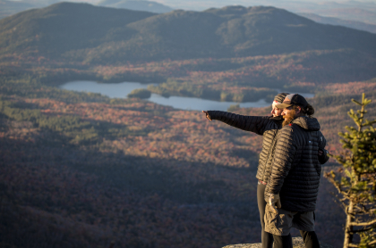 Two people enjoy a fall view from a mountain top