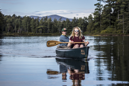Two people canoeing on a lake surrounded by trees