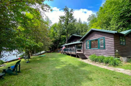 Lush green lawn next to blue waters of Lake Flower highlight the dark stain on this Log cabin by the lake.