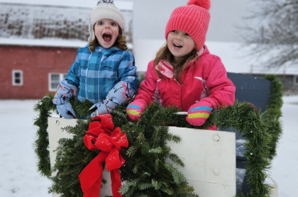 Two very happy young girls in a sled with garland and wreaths with red bows.