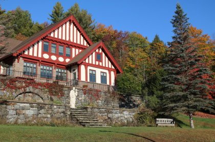 The large lawn with bench and stone walls in front of the Swiss inspired building; white with read trim.