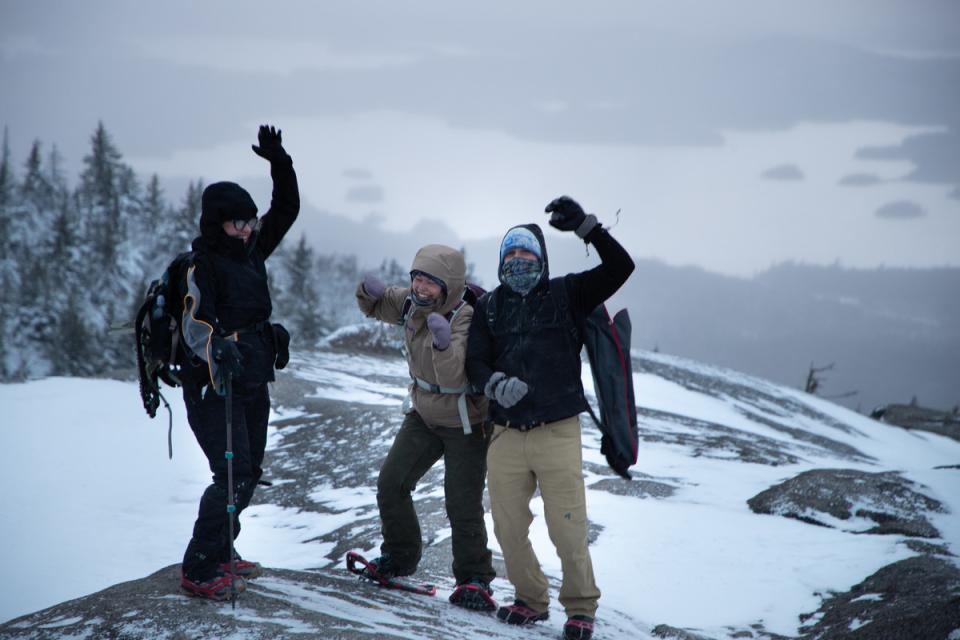 Three hikers cheering at the summit of Ampersand Mountain in the winter