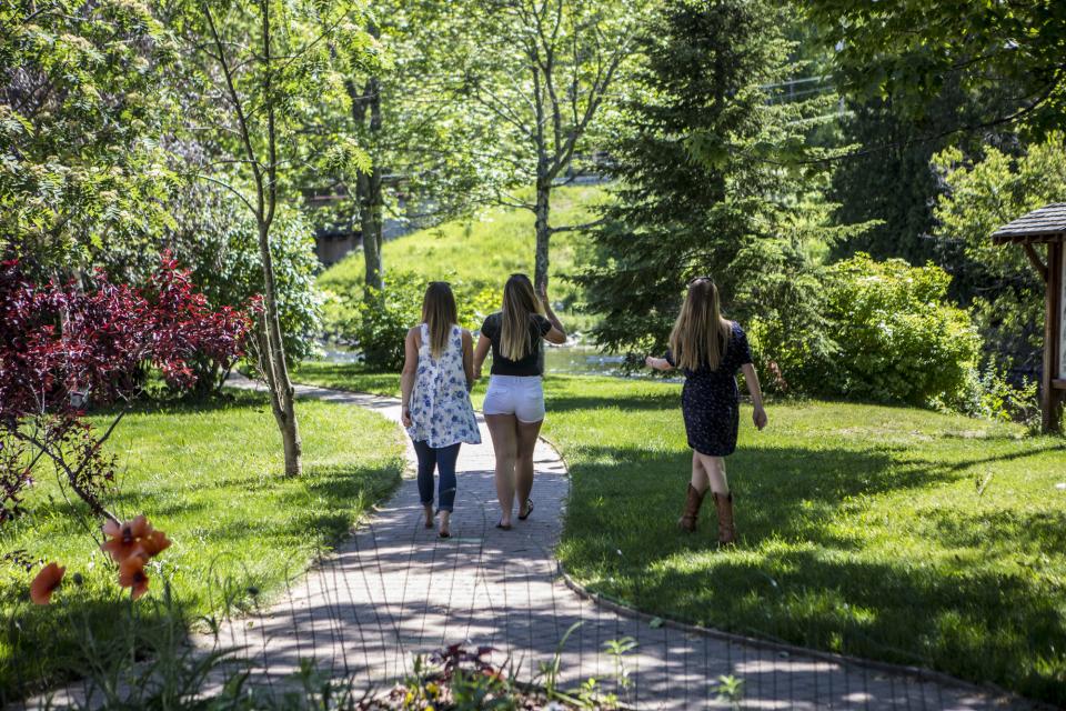 Three girls walk along the stone path of the Saranac Lake Riverwalk on a beautiful summer day.