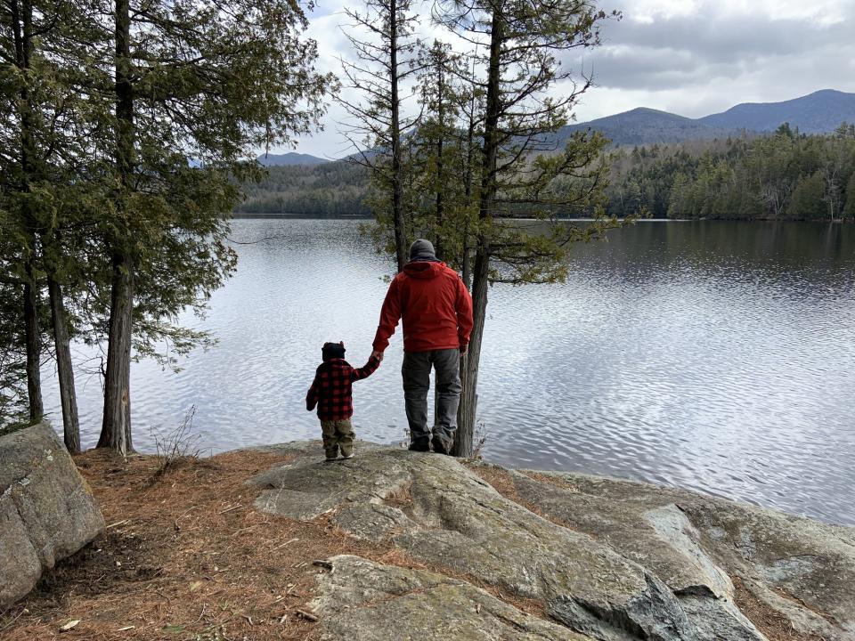 Father and son hold hands as they walk over a rock near the shoreline of Moose Pond