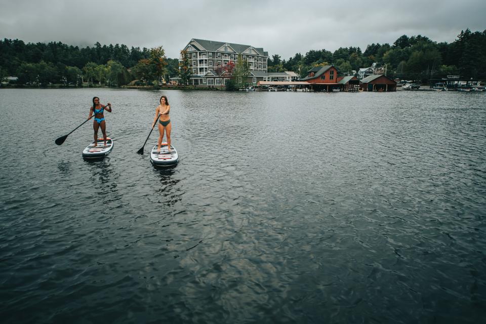 Two paddleboarders on Lake Flower with Saranac Waterfront Lodge in the background