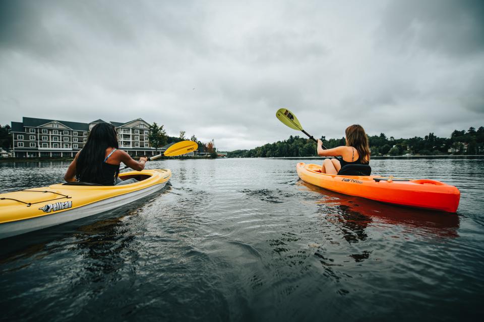 Two women kayaking on Lake Flower with Saranac Waterfront Lodge in the background