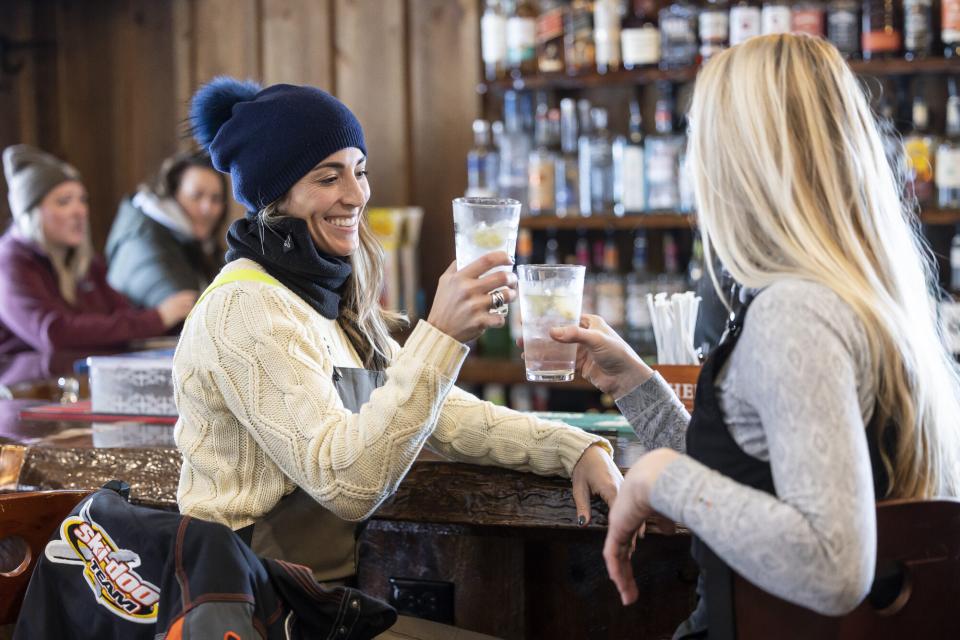 two women in snow suits cheers at the bar.