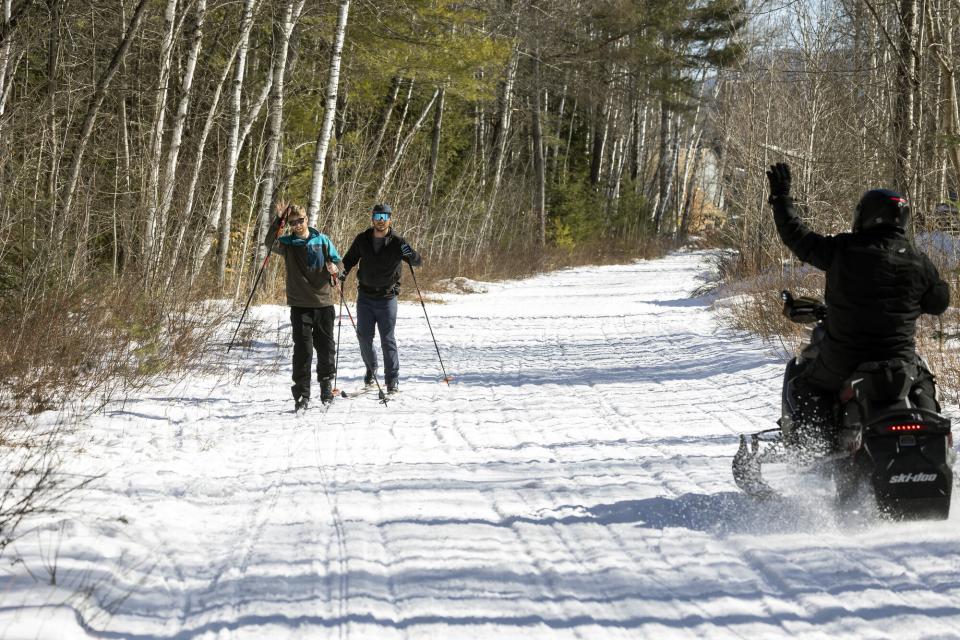 Skiers pass a snowmobiler on a trail.