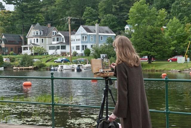 ​​A woman paints at an easel at the shore of Lake Flower during the Plein Air Festival, one of the Adirondack art shows in Saranac Lake