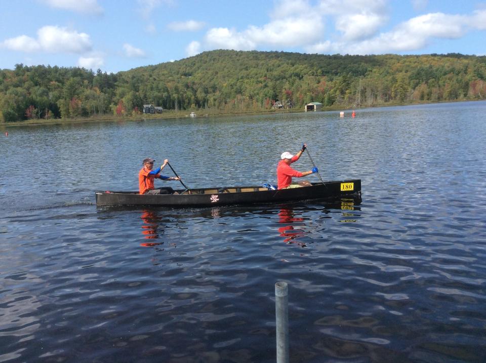 Two men paddle a black canoe across a lake during the Adirondack 90-Miler