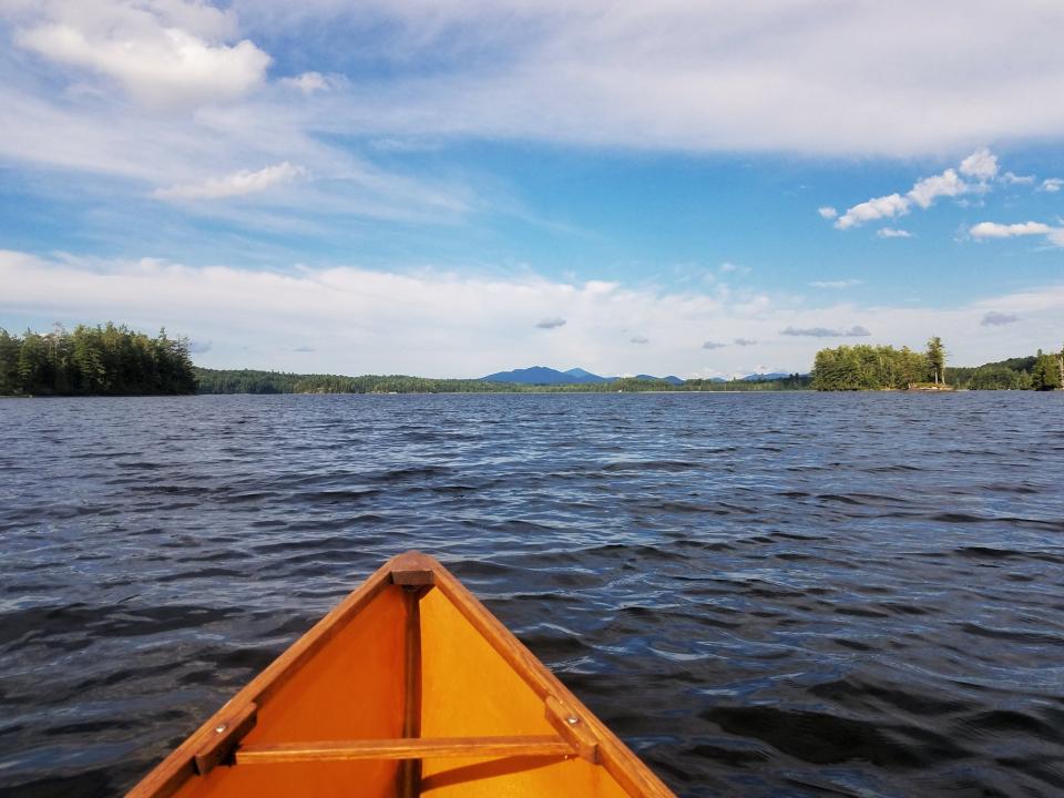 The bow of a canoe on an Adirondack lake with water and mountain views.