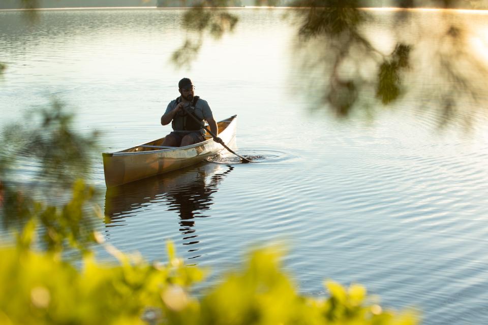 Photograph of a man paddling along a peaceful lake in a canoe