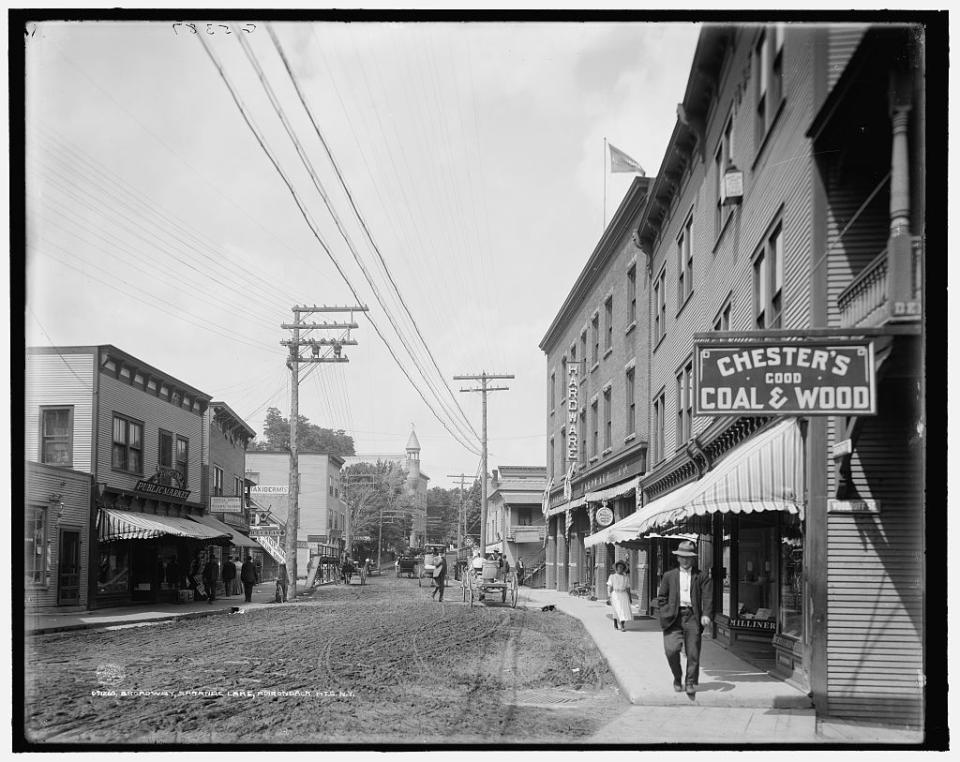A black and white view, circa 1909, of Broadway shops and dirt street.