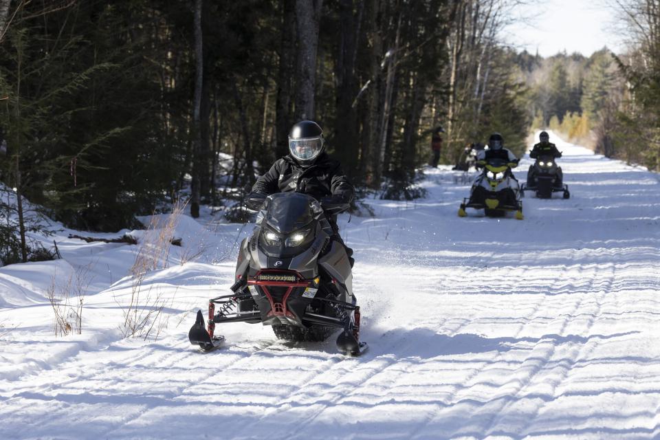 A line of snowmobilers travel on a trail.