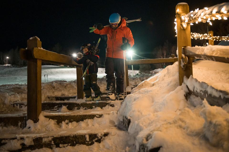 An adult and a child carry skis at Mt Pisga on a winter's night