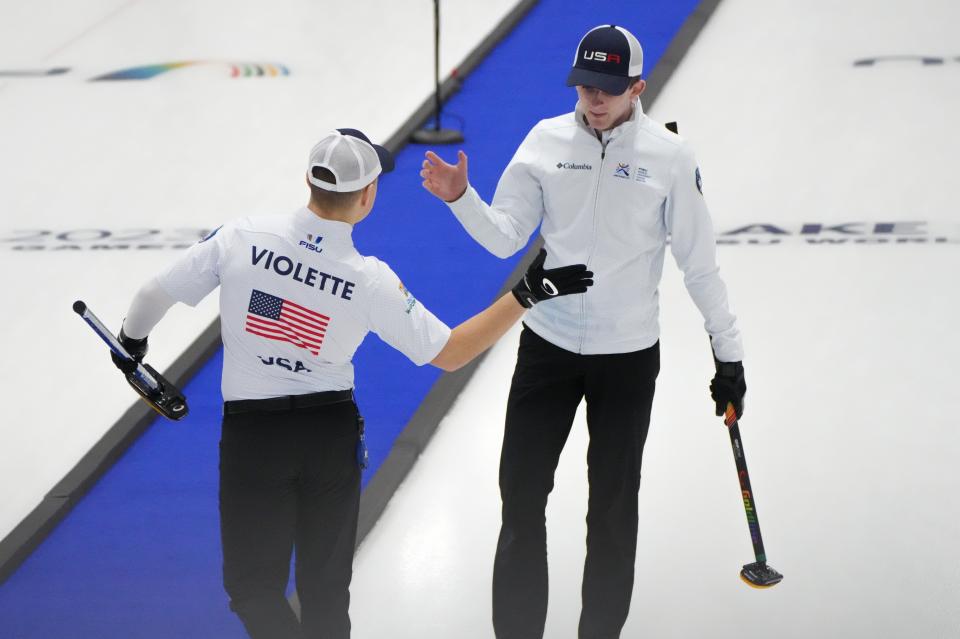 Two male curling athletes extend their hands for a "high five"